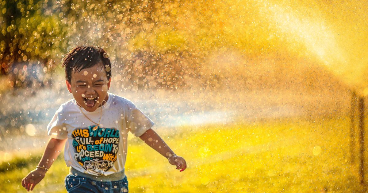 young boy smiling while running through a sprinkler